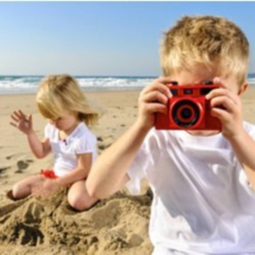 junge fotografiert mit roter kinderkamera am strand