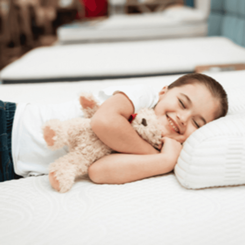 kleines Kind mit Teddybär auf einer Matratze