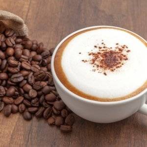 Tasse Kaffee mit in Milchaufschäumer aufgeschlagenem Schaum neben Kaffeebohnen