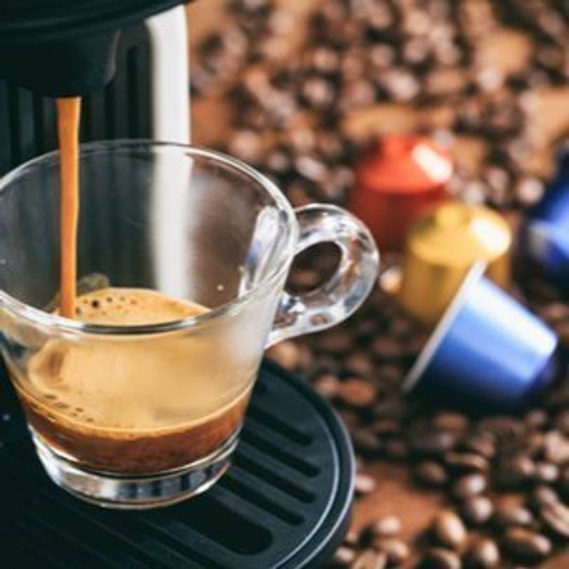 Kaffee aus einer Nespresso-Maschine und Nespresso-Kapseln im Hintergrund