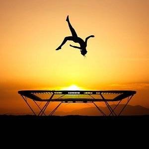 Frau, die auf Trampolin sehr hoch springt vor Sonnenuntergang