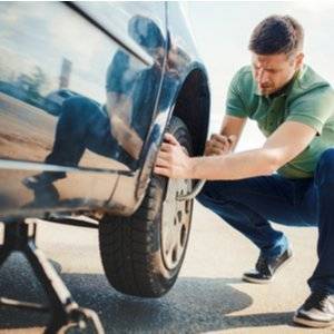 Mann, der Reifen wechselt, während Auto von Wagenheber gehalten wird